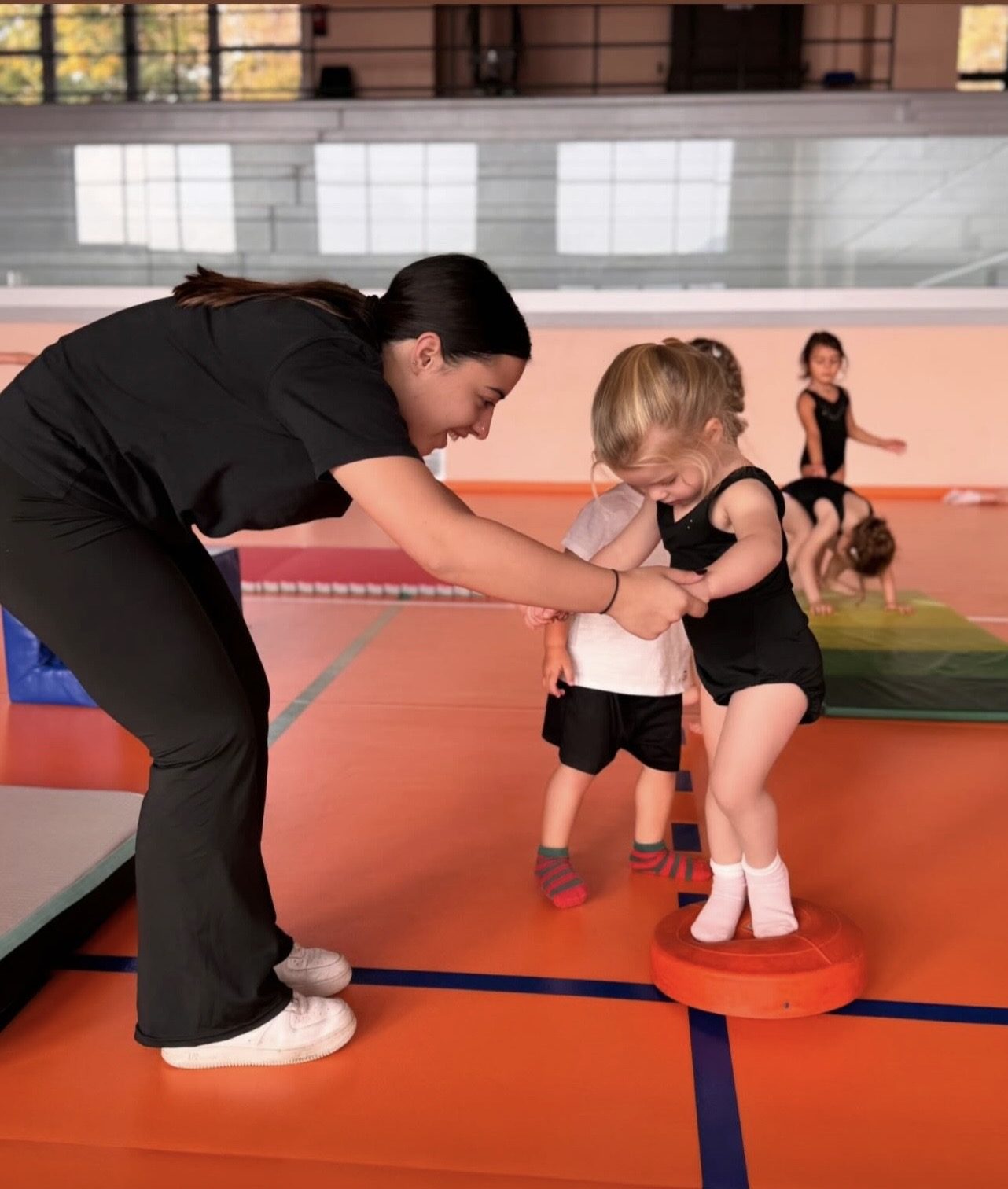 Insegnante accompagna due bambini nei primi esercizi di equilibrio in palestra